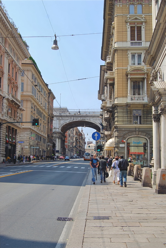 29 - Via XX Settembre in Genoa, featuring its signature grand 19th-century architecture, elegant sidewalk arcades, and the iconic Ponte Monumentale arching across the boulevard